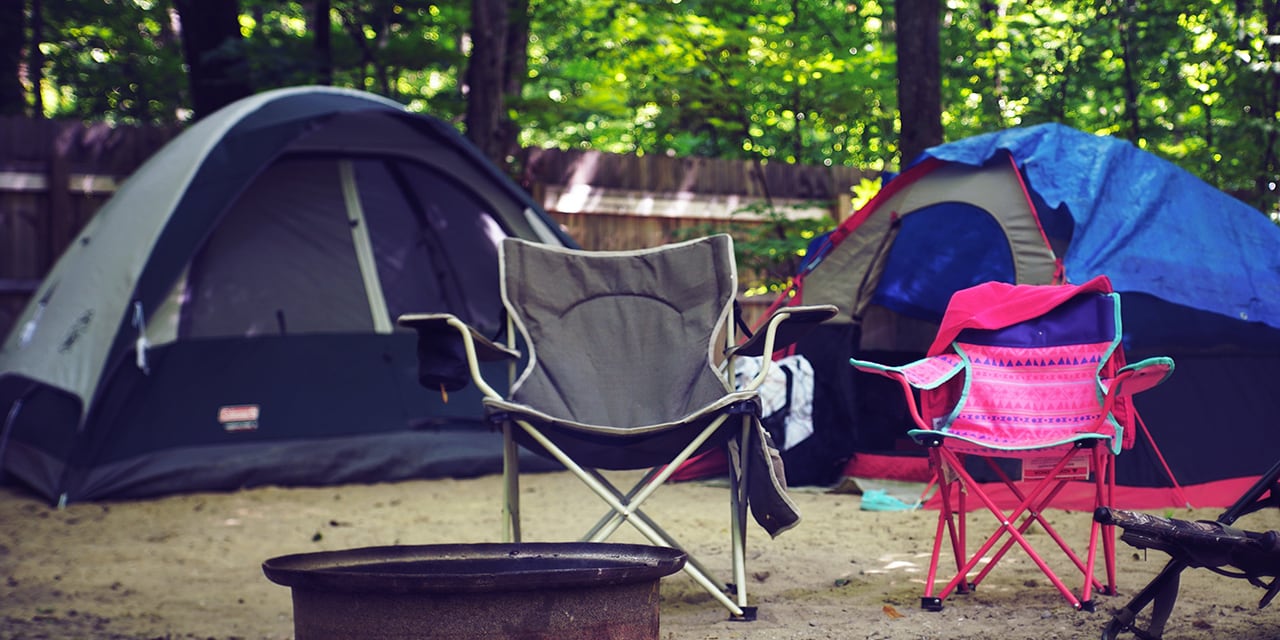 Two camping tents, both shades of blue in colour, with a grey and pink camping chair in the foreground