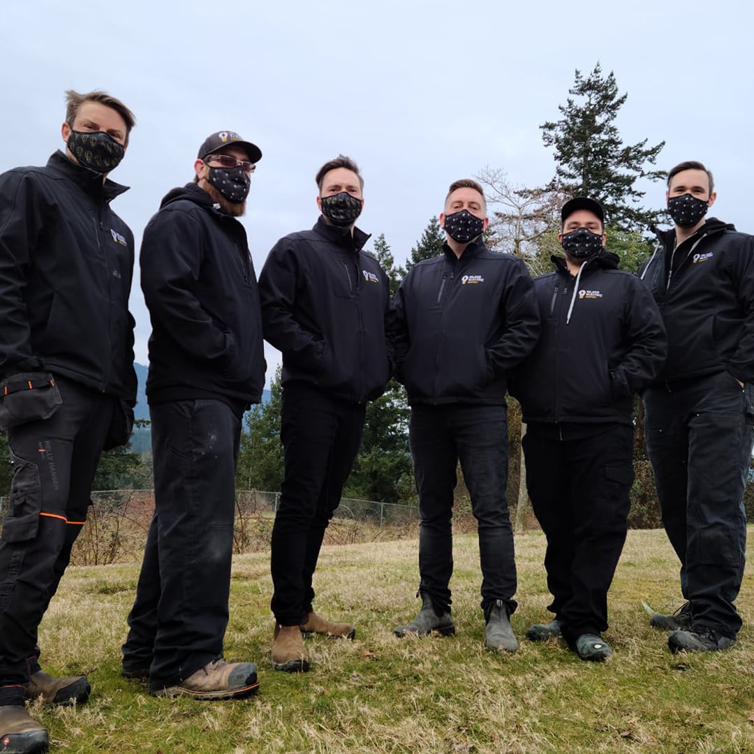 Low-angle view of the Island Electric staff, dressed in black jackets with company logos, and all staff wearing black face coverings